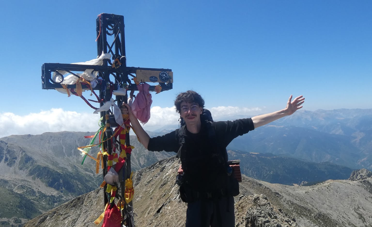 Antonin Hérault touchant le croix du Pic du Canigou avec une vue dégagée sur les Pyrénées