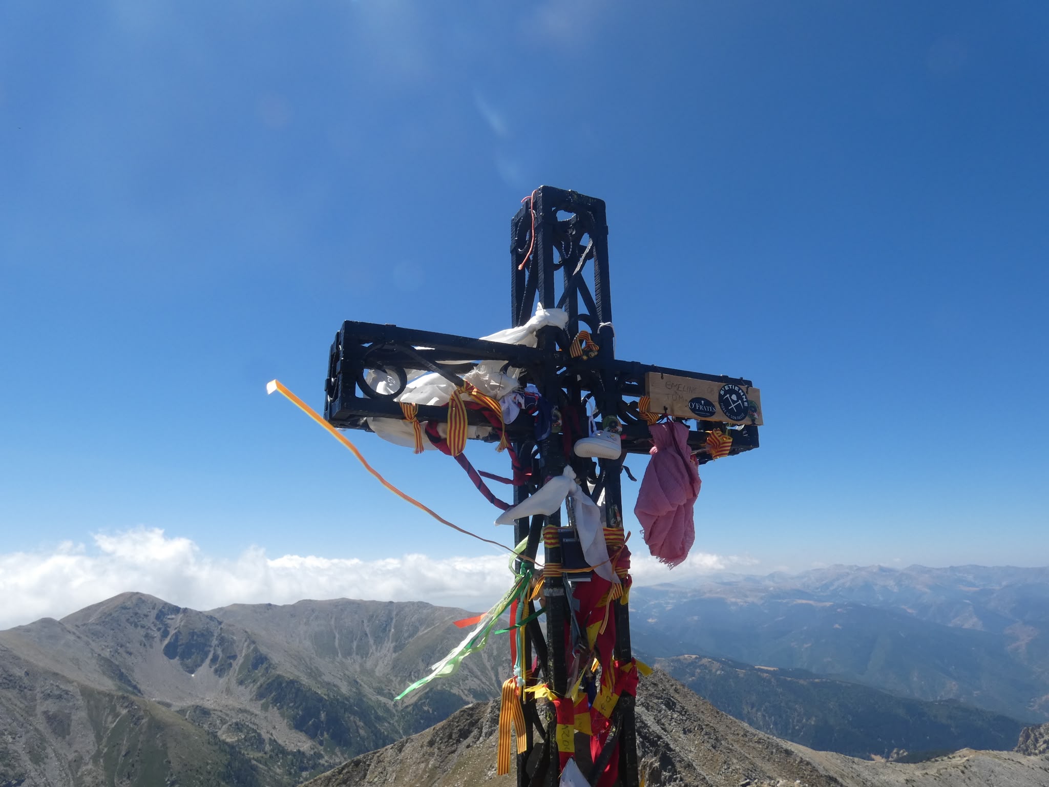Croix chrétienne couverte de bouts de tissus dont des drapeaux catalans avec une vue sur les Pyrénées