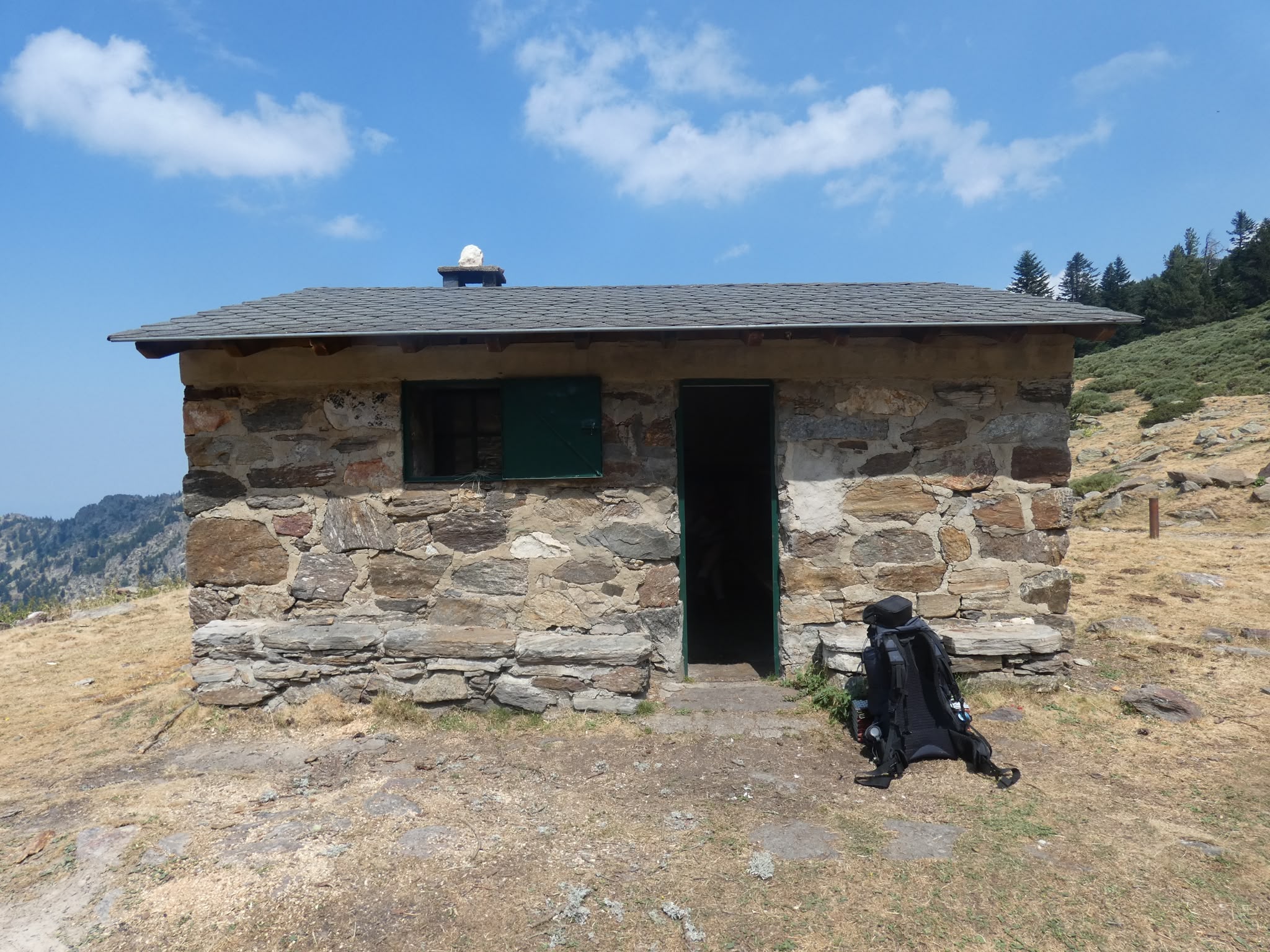 Une petite maison en pierre dans la montagne avec un sac à dos posé devant